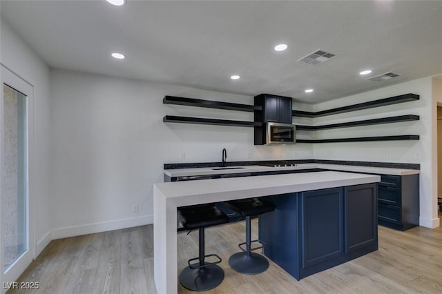 7132 Mission Hills Dr, Las Vegas, NV 89113 - kitchen with open shelves, stainless steel microwave, light wood-style floors, a kitchen breakfast bar, and a kitchen island