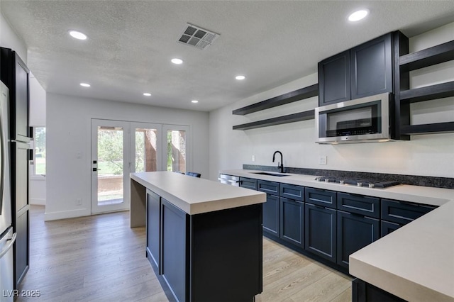 7132 Mission Hills Dr, Las Vegas, NV 89113 - kitchen with open shelves, appliances with stainless steel finishes, light wood-type flooring, a center island, and light countertops