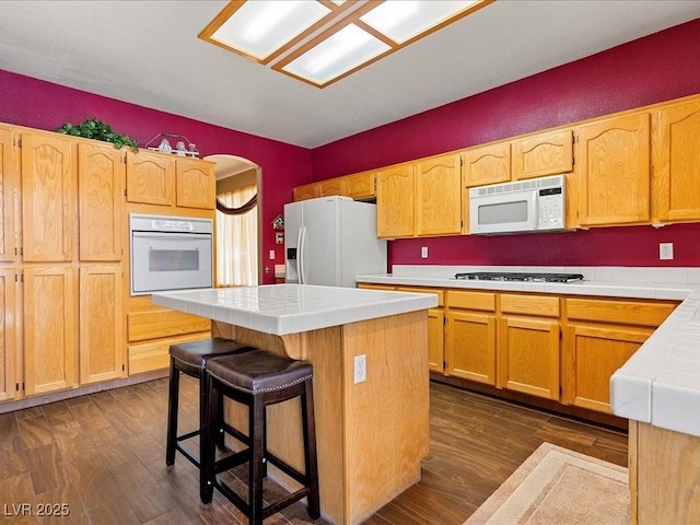 1870 Desert Forest Way, Henderson, NV 89012 - kitchen with white appliances, tile counters, a kitchen island, dark wood-style flooring, and a kitchen bar