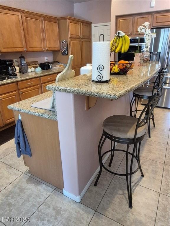 6009 Arbor Crest St, North Las Vegas, NV 89081 - kitchen with stainless steel appliances, a kitchen island, a kitchen bar, brown cabinetry, and light tile patterned floors