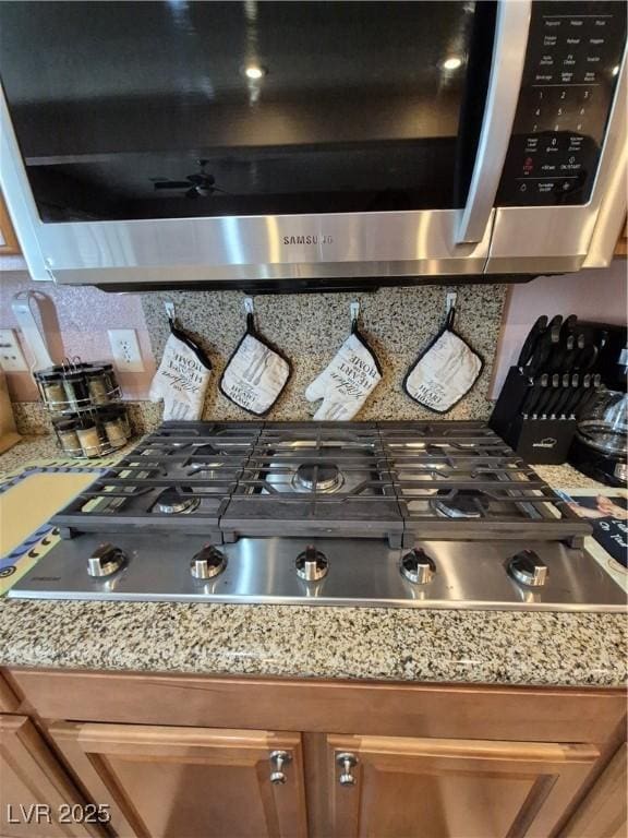6009 Arbor Crest St, North Las Vegas, NV 89081 - detailed view of appliances with stainless steel finishes, backsplash, brown cabinetry, ceiling fan, and light stone counters