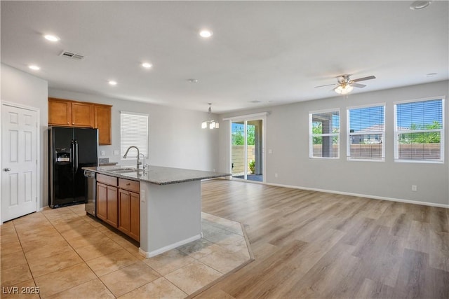9136 Cocowoods Pl, Las Vegas, NV 89148 - kitchen with black fridge, stainless steel dishwasher, open floor plan, a kitchen island with sink, and stone countertops