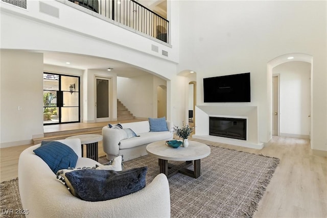 9408 Players Canyon Ct, Las Vegas, NV 89144 - living room featuring wood finished floors, a high ceiling, a glass covered fireplace, stairs, and arched walkways