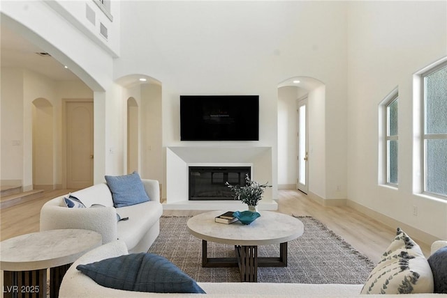 9408 Players Canyon Ct, Las Vegas, NV 89144 - living area featuring wood finished floors, a high ceiling, healthy amount of natural light, a glass covered fireplace, and arched walkways