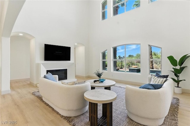 9408 Players Canyon Ct, Las Vegas, NV 89144 - living area featuring a high ceiling, arched walkways, light wood-style floors, healthy amount of natural light, and a glass covered fireplace