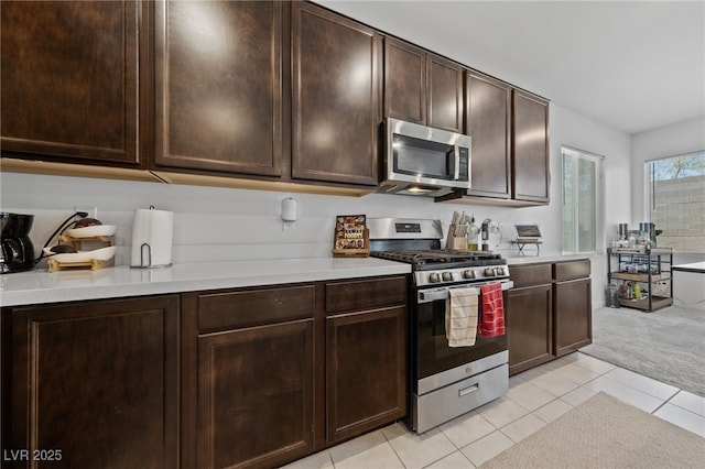 2732 Roman Palm Rd, North Las Vegas, NV 89086 - kitchen with stainless steel appliances, light countertops, light tile patterned floors, light colored carpet, and dark brown cabinetry
