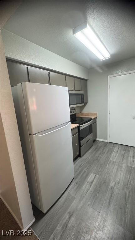 8101 W Flamingo Rd Unit 2110, Las Vegas, NV 89147 - kitchen featuring stainless steel appliances, light wood finished floors, gray cabinetry, a textured ceiling, and light countertops