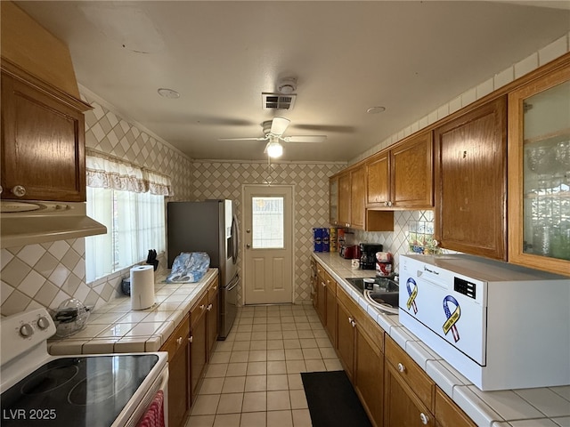 4567 S Nellis Blvd, Las Vegas, NV 89121 - kitchen with tile counters, white range with electric cooktop, wallpapered walls, stainless steel fridge with ice dispenser, and brown cabinetry