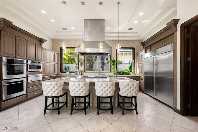 9325 Canyon Classic Dr, Las Vegas, NV 89144 - kitchen featuring appliances with stainless steel finishes, a warming drawer, island range hood, an island with sink, and light stone counters