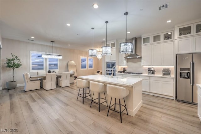 8984 Rolling Pietra St, Las Vegas, NV 89166 - kitchen with appliances with stainless steel finishes, wall chimney range hood, light wood finished floors, white cabinetry, and a center island with sink