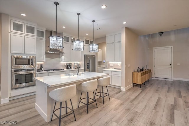 8984 Rolling Pietra St, Las Vegas, NV 89166 - kitchen with appliances with stainless steel finishes, wall chimney range hood, light wood-type flooring, light countertops, and a breakfast bar area