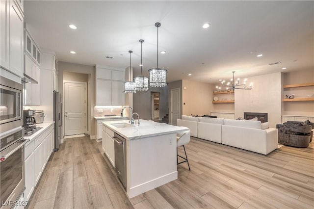 8984 Rolling Pietra St, Las Vegas, NV 89166 - kitchen with a chandelier, appliances with stainless steel finishes, light wood-style flooring, white cabinetry, and a kitchen island with sink