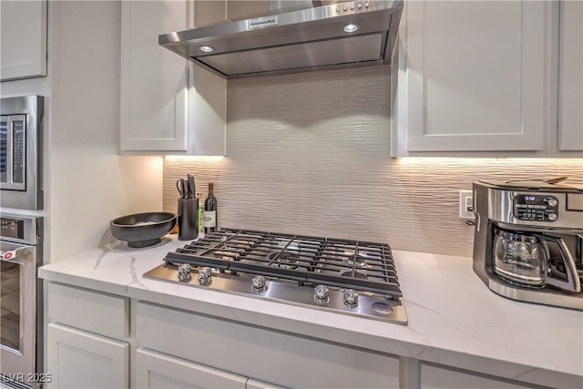 8984 Rolling Pietra St, Las Vegas, NV 89166 - kitchen with appliances with stainless steel finishes, range hood, decorative backsplash, light stone counters, and white cabinets