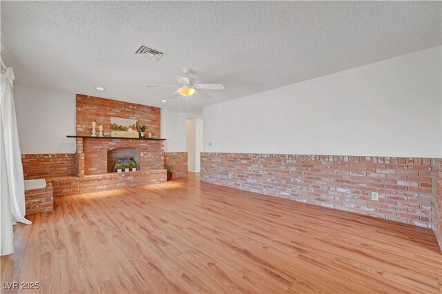 1705 Westwind Rd, Las Vegas, NV 89146 - unfurnished living room featuring wood finished floors, a textured ceiling, ceiling fan, brick wall, and a brick fireplace