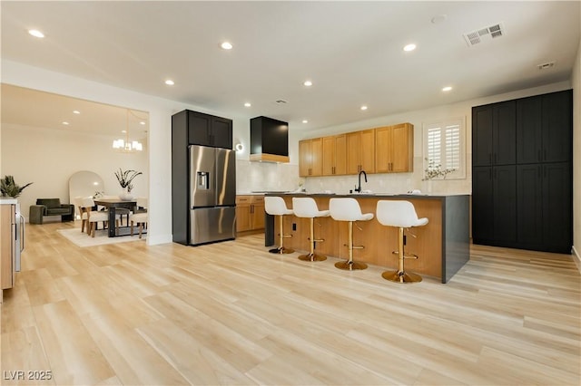 4493 Rometta Ave, Las Vegas, NV 89141 - kitchen with stainless steel fridge, wall chimney range hood, backsplash, a kitchen breakfast bar, and light wood-style floors