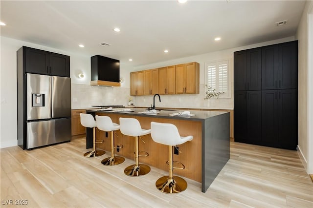 4493 Rometta Ave, Las Vegas, NV 89141 - kitchen with appliances with stainless steel finishes, wall chimney range hood, a center island with sink, backsplash, and light wood-style flooring