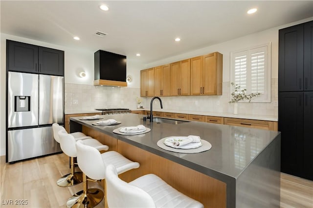 4493 Rometta Ave, Las Vegas, NV 89141 - kitchen featuring stainless steel fridge, wall chimney range hood, an island with sink, backsplash, and recessed lighting