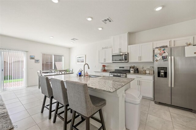 7730 Moore Creek Ln, North Las Vegas, NV 89084 - kitchen featuring stainless steel appliances, light tile patterned floors, a kitchen island with sink, a breakfast bar area, and white cabinetry