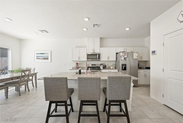 7730 Moore Creek Ln, North Las Vegas, NV 89084 - kitchen with appliances with stainless steel finishes, a breakfast bar area, light tile patterned floors, white cabinetry, and light stone counters