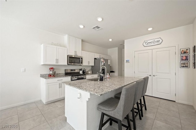 7730 Moore Creek Ln, North Las Vegas, NV 89084 - kitchen featuring appliances with stainless steel finishes, light tile patterned floors, white cabinetry, a kitchen bar, and recessed lighting