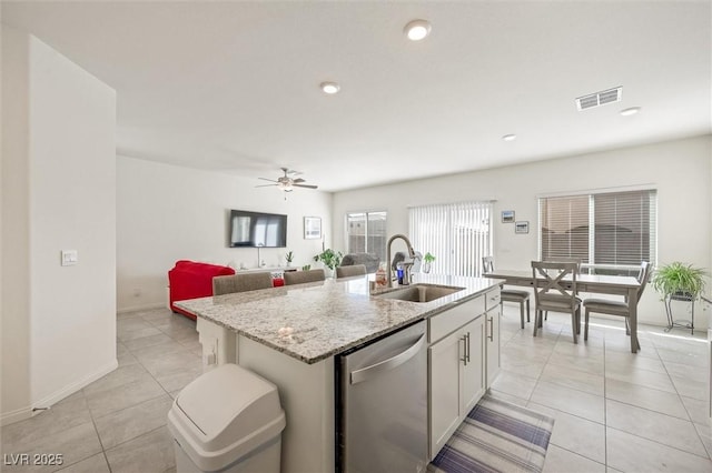 7730 Moore Creek Ln, North Las Vegas, NV 89084 - kitchen with stainless steel dishwasher, light tile patterned floors, a center island with sink, ceiling fan, and light stone counters