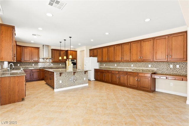 2755 Asgard Ave, Las Vegas, NV 89121 - kitchen featuring wall chimney range hood, white refrigerator with ice dispenser, brown cabinets, decorative backsplash, and light stone countertops