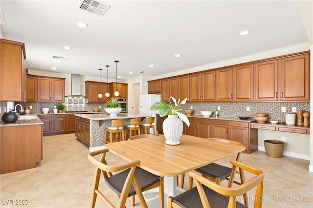 2755 Asgard Ave, Las Vegas, NV 89121 - kitchen with wall chimney range hood, stainless steel oven, a center island, brown cabinetry, and tasteful backsplash
