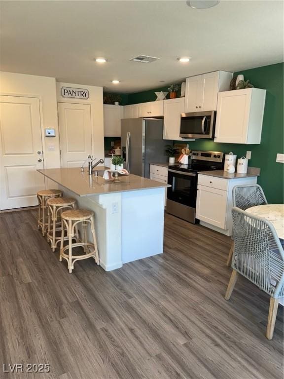 1900 Arietta Vista St, Henderson, NV 89044 - kitchen featuring appliances with stainless steel finishes, dark wood-style floors, white cabinets, an island with sink, and a breakfast bar area