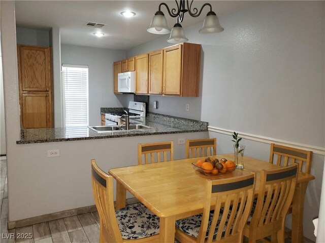 6283 Lapilli Ave, Las Vegas, NV 89139 - kitchen featuring white appliances, a peninsula, light wood-style flooring, dark stone counters, and pendant lighting
