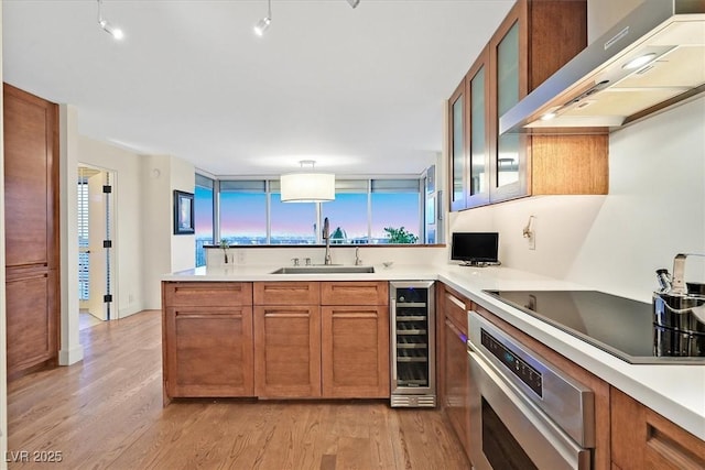3111 Bel Air Dr Unit 7D, Las Vegas, NV 89109 - kitchen with range hood, wine cooler, stainless steel oven, black electric cooktop, and brown cabinetry