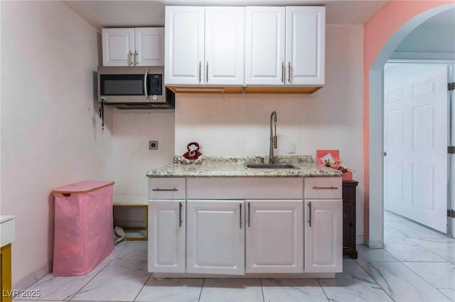 2990 Carnelian St, Las Vegas, NV 89121 - kitchen featuring stainless steel microwave, light marble finish flooring, arched walkways, and white cabinets