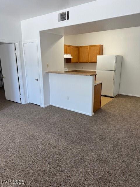 2019 Rancho Lake Dr Unit 102, Las Vegas, NV 89108 - kitchen with freestanding refrigerator, light carpet, under cabinet range hood, a peninsula, and brown cabinets