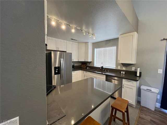3736 Steinbeck Dr, Las Vegas, NV 89115 - kitchen featuring appliances with stainless steel finishes, dark countertops, white cabinetry, rail lighting, and a textured ceiling