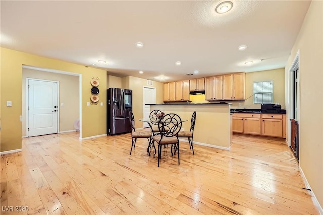 3168 Via Festiva, Henderson, NV 89044 - kitchen with black fridge with ice dispenser, light brown cabinets, light wood-style flooring, dark countertops, and under cabinet range hood