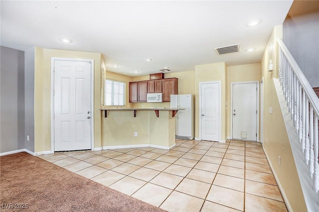 3905 Sweet Pine St Unit 102, Las Vegas, NV 89108 - kitchen featuring white appliances, a kitchen bar, a peninsula, light tile patterned floors, and recessed lighting