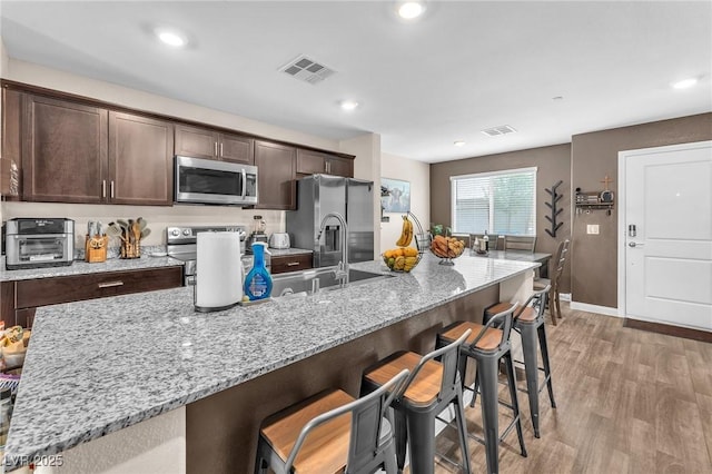 12280 Golden Wreath Rd Unit 3, Las Vegas, NV 89183 - kitchen featuring appliances with stainless steel finishes, dark brown cabinets, a kitchen bar, light wood-style flooring, and light stone counters