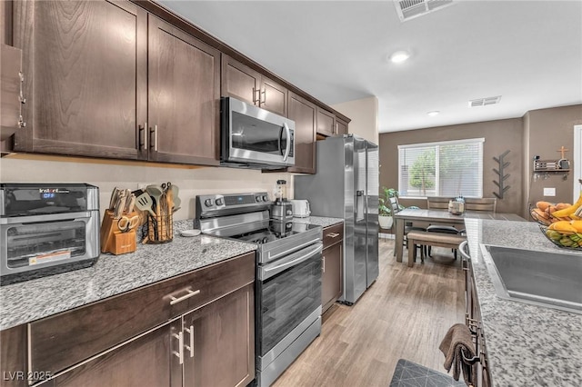 12280 Golden Wreath Rd Unit 3, Las Vegas, NV 89183 - kitchen featuring stainless steel appliances, dark brown cabinetry, light wood-style floors, light stone counters, and recessed lighting