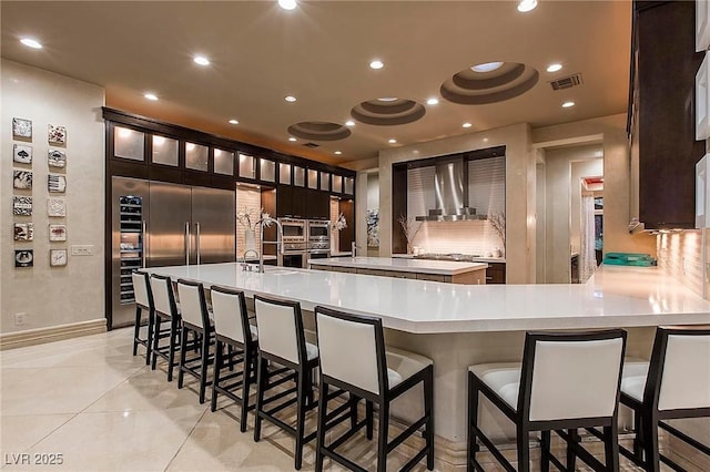 15 Golden Sunray Ln, Las Vegas, NV 89135 - kitchen with wall chimney range hood, light countertops, a kitchen bar, built in refrigerator, and a large island with sink