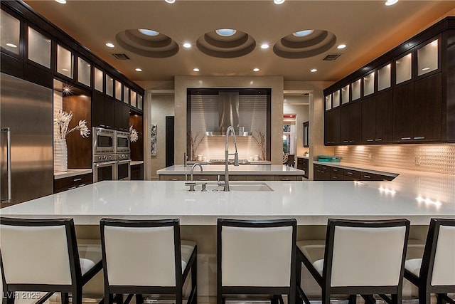 15 Golden Sunray Ln, Las Vegas, NV 89135 - kitchen with light countertops, built in appliances, a center island with sink, glass insert cabinets, and recessed lighting