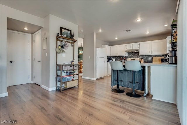 1048 Menands Ave, Las Vegas, NV 89123 - kitchen with freestanding refrigerator, white cabinets, under cabinet range hood, light wood-type flooring, and backsplash