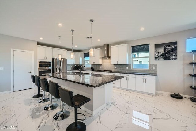 6834 Compass St, North Las Vegas, NV 89084 - kitchen with wall chimney range hood, stainless steel appliances, decorative backsplash, an island with sink, and white cabinetry