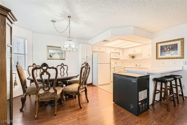 1104 Pinto Rock Ln Unit 101, Las Vegas, NV 89128 - kitchen with white appliances, a chandelier, a peninsula, a textured ceiling, and wood finished floors