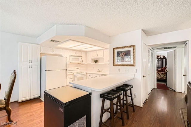 1104 Pinto Rock Ln Unit 101, Las Vegas, NV 89128 - kitchen with white appliances, dark wood-style flooring, a peninsula, a kitchen breakfast bar, and light countertops