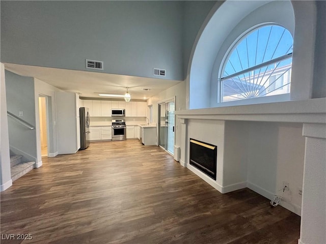 6063 Peach Orchard Rd, Las Vegas, NV 89142 - unfurnished living room with dark wood-style flooring, a fireplace, stairs, and a towering ceiling