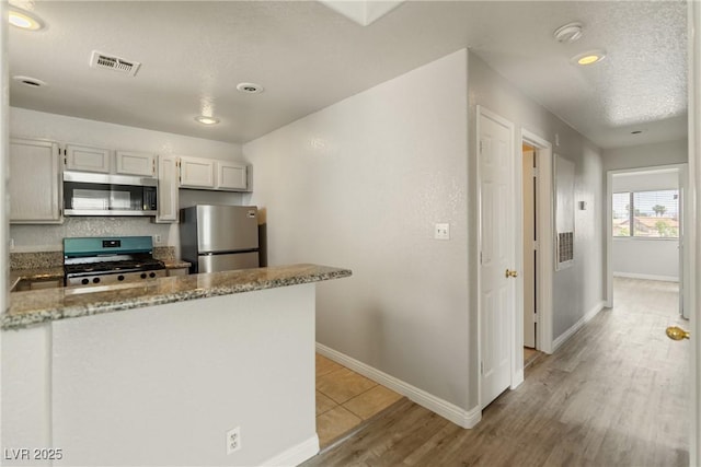 5038 S Rainbow Blvd Unit 206, Las Vegas, NV 89118 - kitchen with stainless steel appliances, light wood-style floors, light stone countertops, and a peninsula