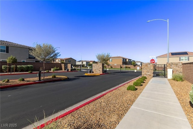 6909 Toll Mountain St, North Las Vegas, NV 89086 - view of asphalt road featuring sidewalks, a gate, street lighting, a residential view, and traffic signs