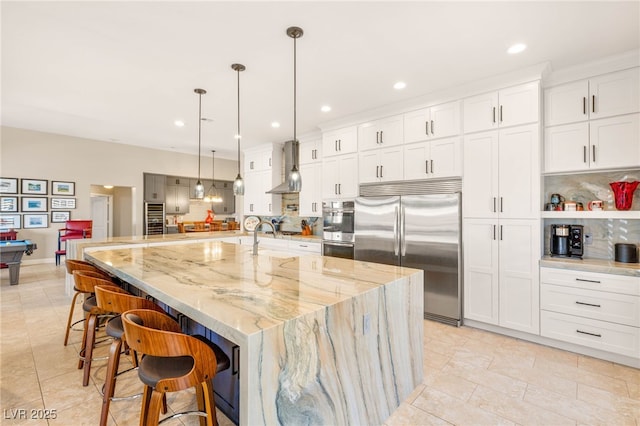 286 Bowsprit Ct, Las Vegas, NV 89183 - kitchen featuring stainless steel appliances, wall chimney range hood, decorative backsplash, white cabinets, and a kitchen bar