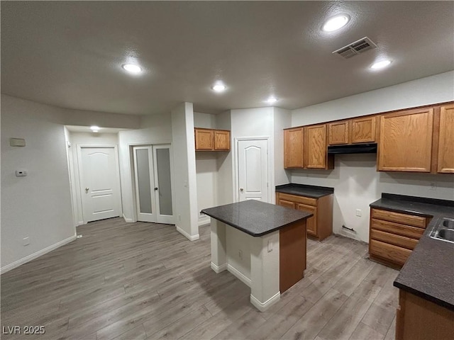 6412 Point Break St, North Las Vegas, NV 89084 - kitchen with brown cabinets, dark countertops, light wood finished floors, range hood, and a center island