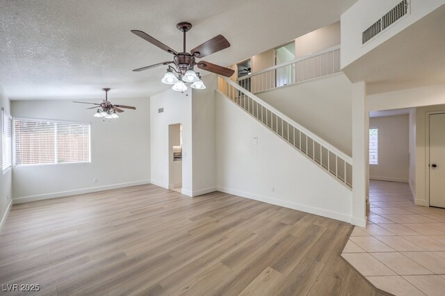 2501 Muirfield Ave, Henderson, NV 89074 - unfurnished living room with a ceiling fan, stairs, light wood-style floors, a textured ceiling, and lofted ceiling