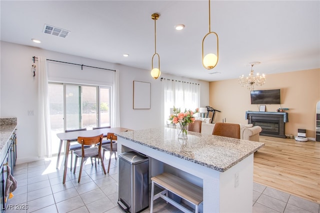 10434 Rose Palisade St, Las Vegas, NV 89141 - kitchen featuring light tile patterned floors, a center island, light stone countertops, a chandelier, and hanging light fixtures